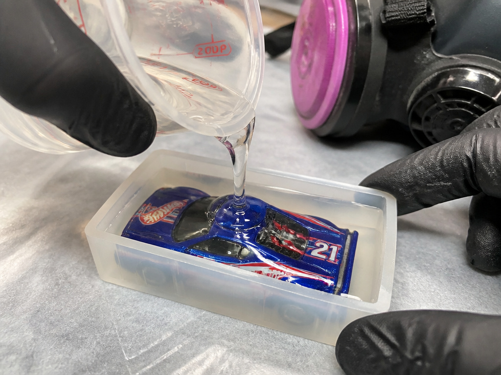 Pouring clear resin over a Hot Wheels car in a silicone mold for a keychain.