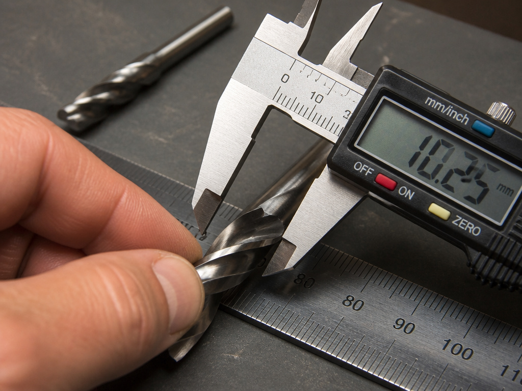 Measuring the flute diameter of a drill bit with calipers to determine its size.