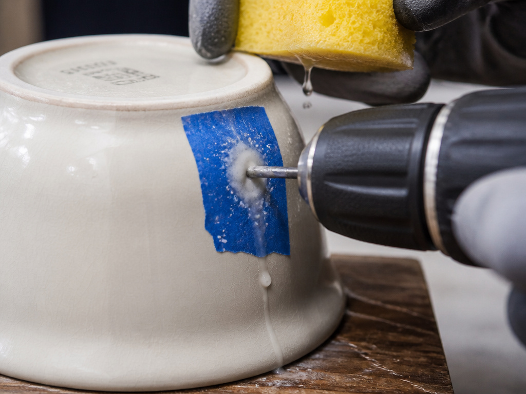 Close-up of drilling a drainage hole in a glazed ceramic pot with water.