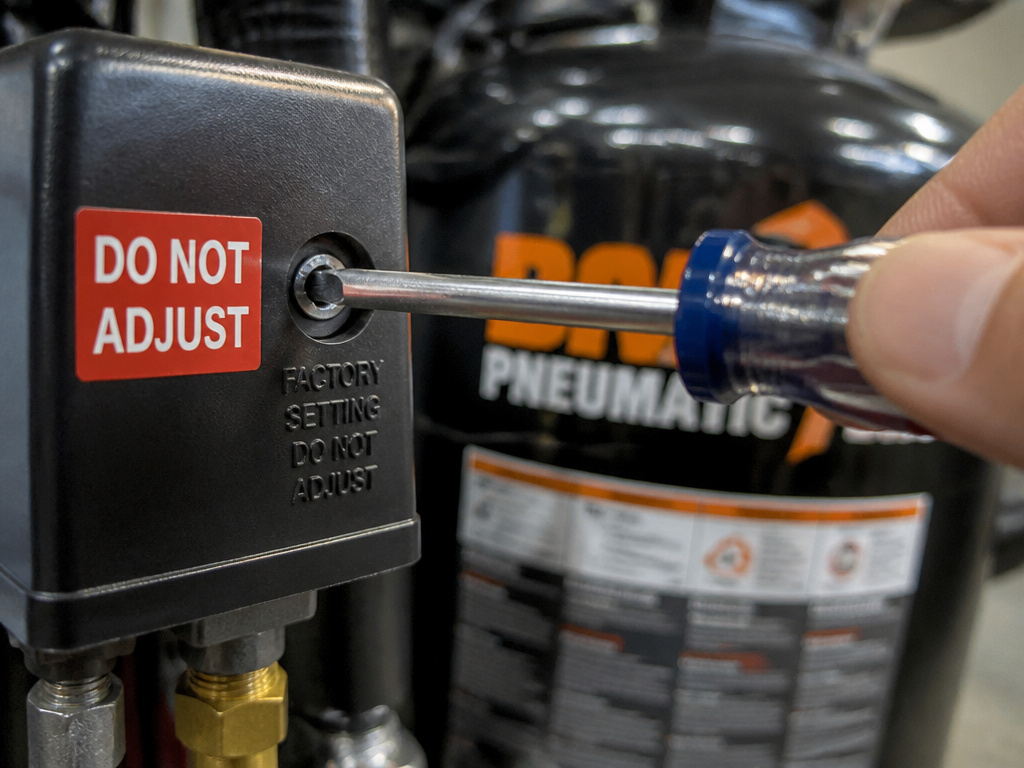 Warning label and sealed adjustment screw on an air compressor pressure switch.